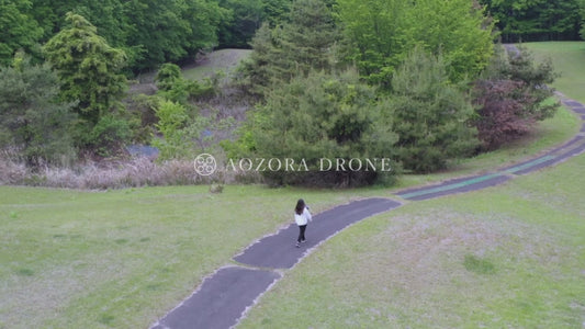 1本の山道をドローン操縦しながら軽快に歩く女性 ドローン空撮動画素材