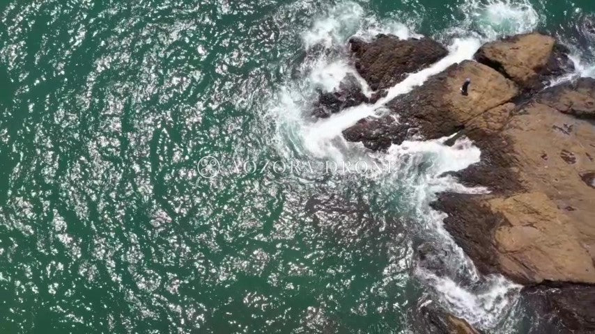 A woman looking at the rough sea from the rocky coast "Akiya no Tateishi" Drone aerial video footage[Kanagawa Prefecture Yokosuka City, Japan]