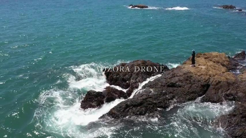 A woman looking at the rough sea from the rocky coast "Akiya no Tateishi" Drone aerial video footage[Kanagawa Prefecture Yokosuka City, Japan]