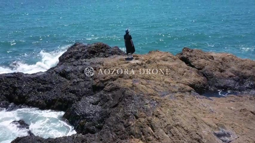 A woman looking at the rough sea at the rocky place of "Akiya no Tateishi" Drone aerial video footage [Kanagawa Prefecture Yokosuka City, Japan]
