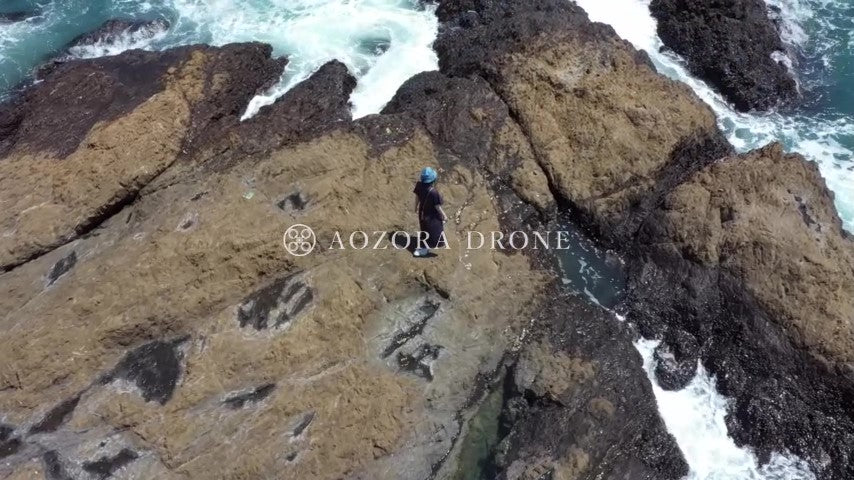 A woman walking towards the sea at the rocky place of "Tateishi of Akiya" Drone aerial video footage [Yokosuka City, Kanagawa Prefecture, Japan]