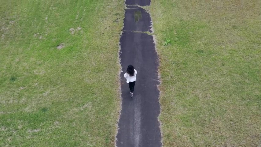 Woman running on a straight road in the forest Drone aerial video footage