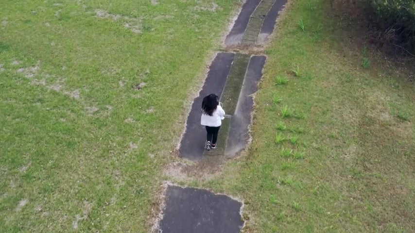 森の中の1本道をランニングする女性 ドローン空撮動画素材